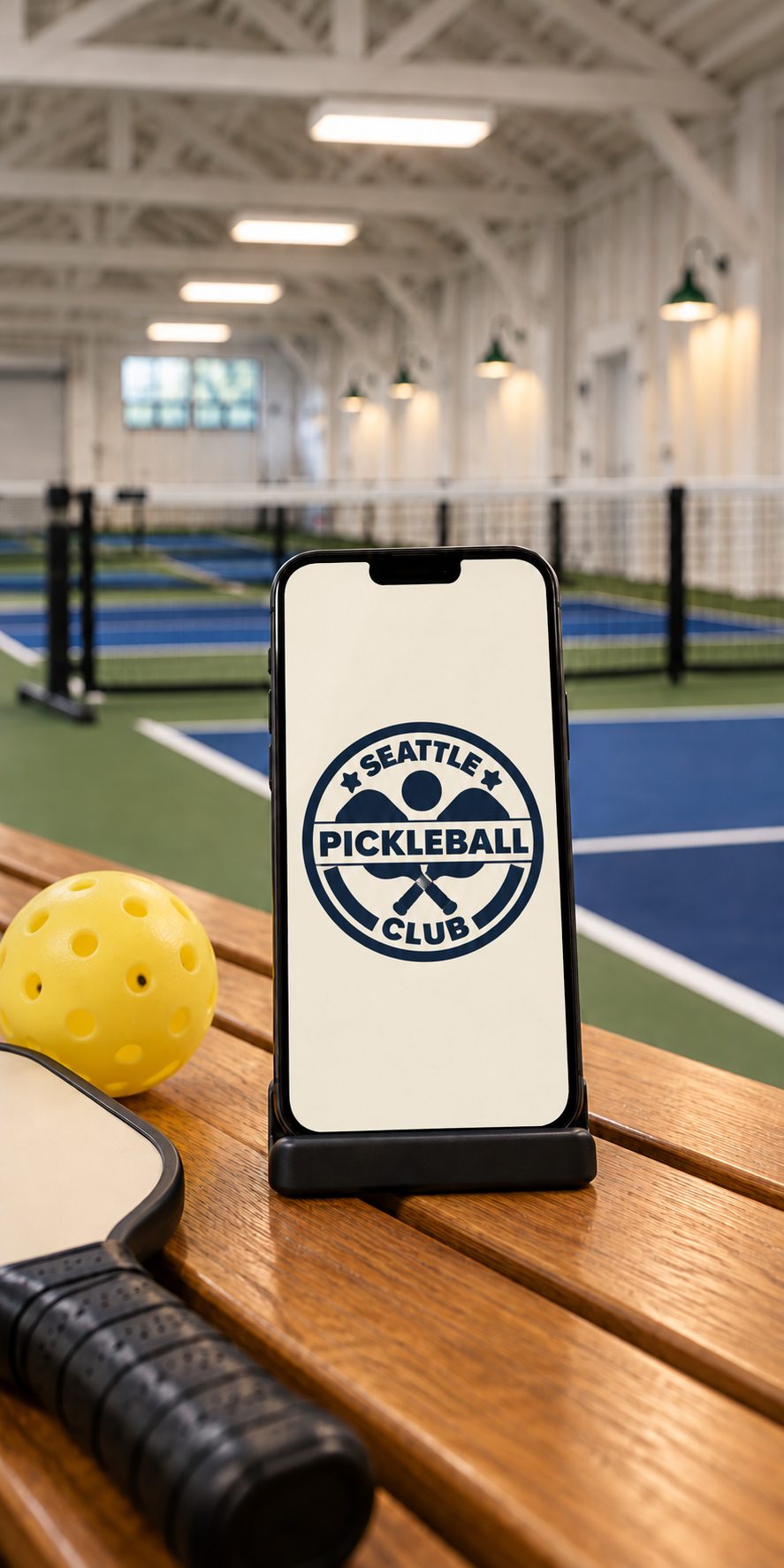 The Seattle Pickleball Club logo on a phone beside a paddle and ball courtside